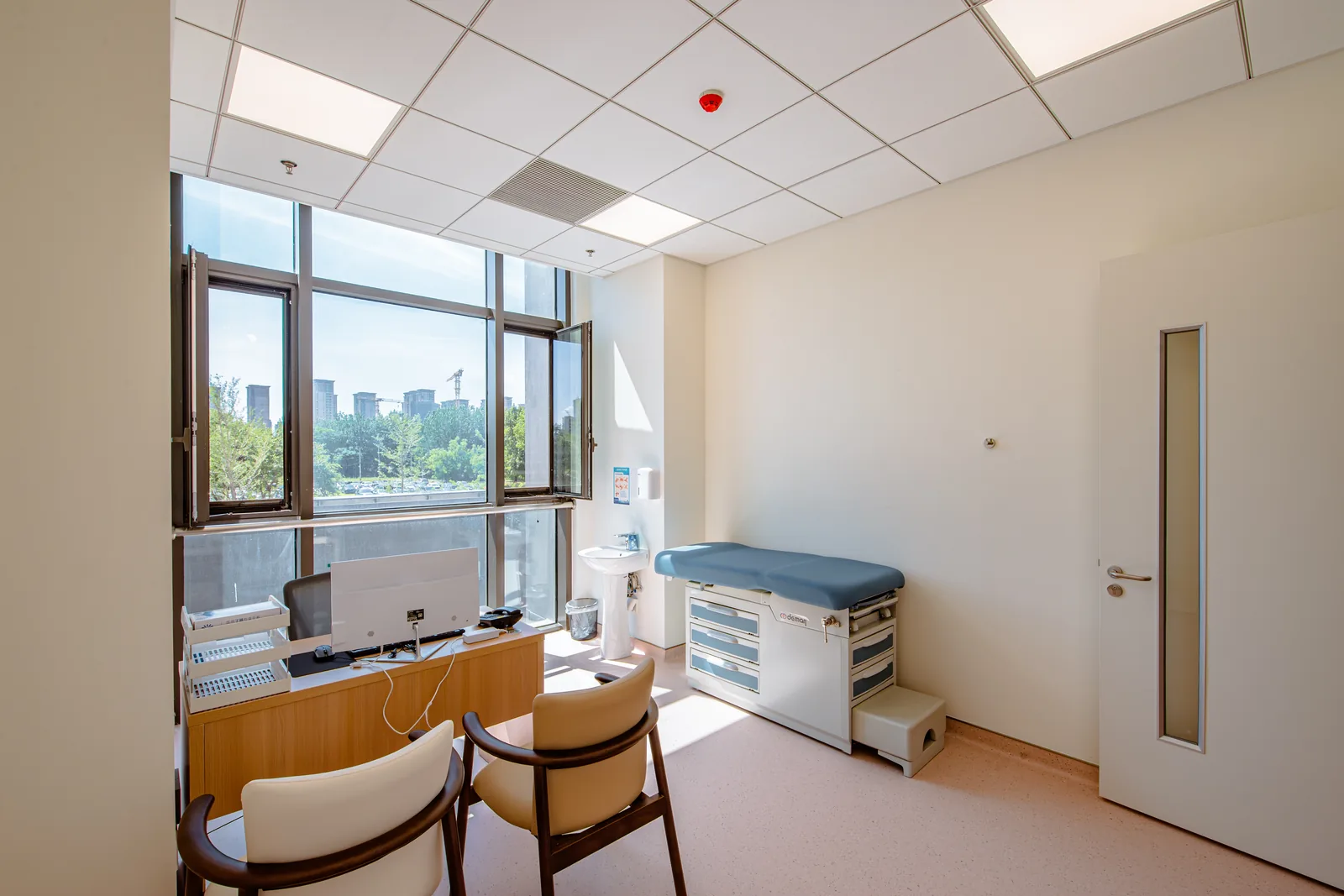 Consultation room with a desk, visitor chairs and an examination couch at Beijing Puhua International Hospital.